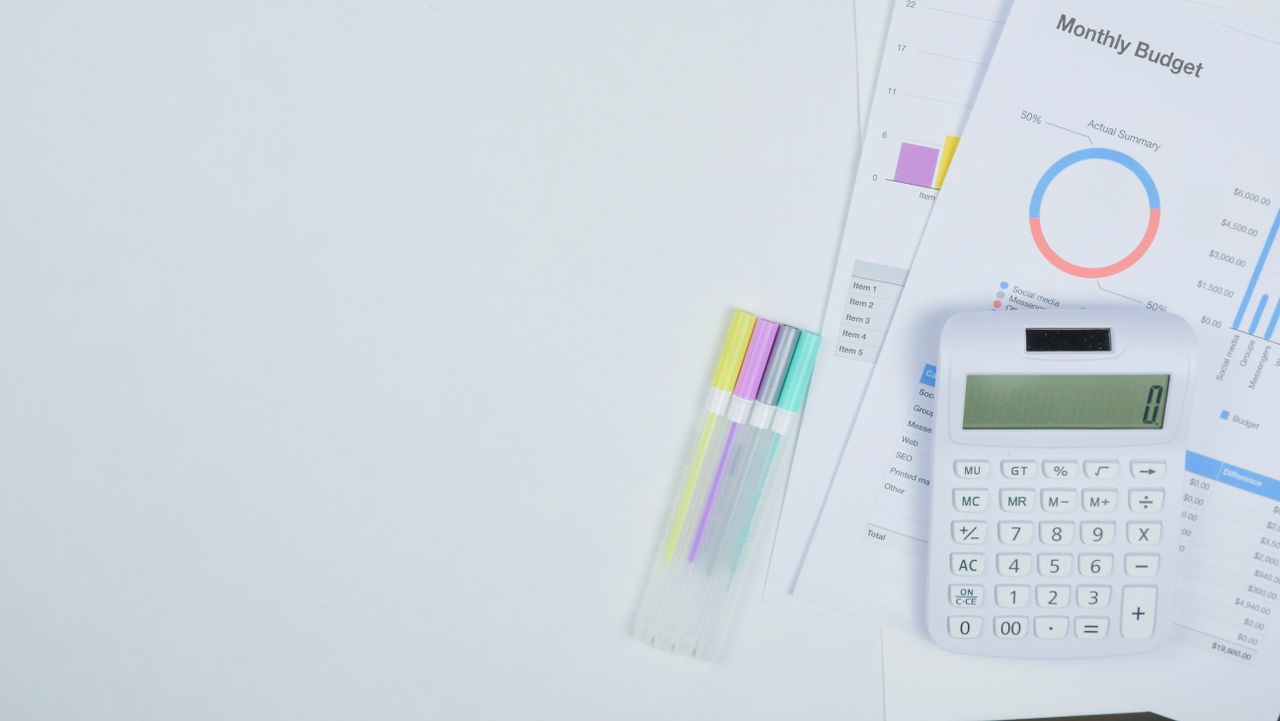 Minimalist office desk with a calculator, budget planning documents, and colorful pens.